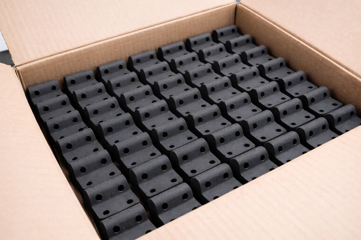 Geöffneter Karton mit einer Serie gleicher schwarzer Bauteile aus PA12, dicht in Reihen gepackt